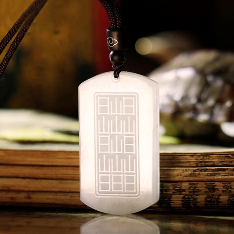 Reverse side of white jade fortune pendant showing engraved grid-style seal pattern and smooth plain jade surface on stacked ancient books