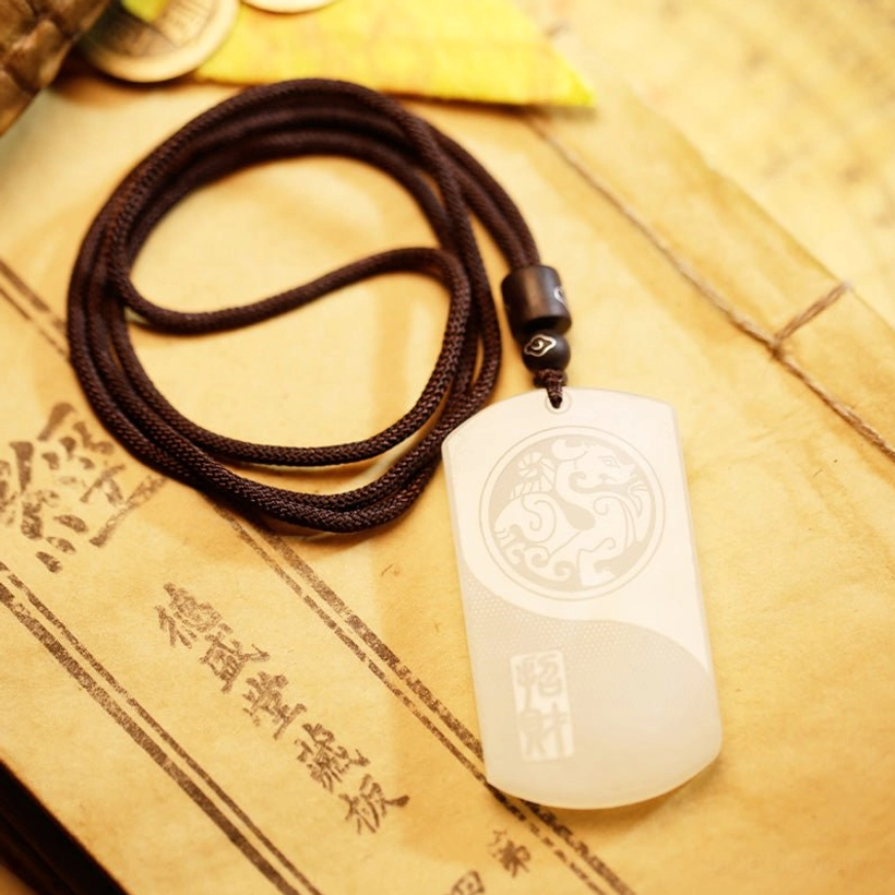 Side view of white jade pendant necklace showing full front engraved pattern with loosely coiled dark cord on ancient book pages