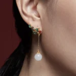 White jade phoenix drop earrings with red agate worn on ear, close-up detail shot showing gold-plated phoenix stud and jade bead