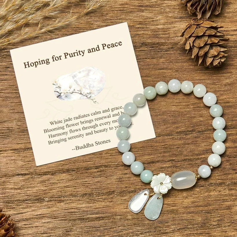 White jade purity bracelet with flower charm and teardrop pendants displayed on wooden table with gift message card
