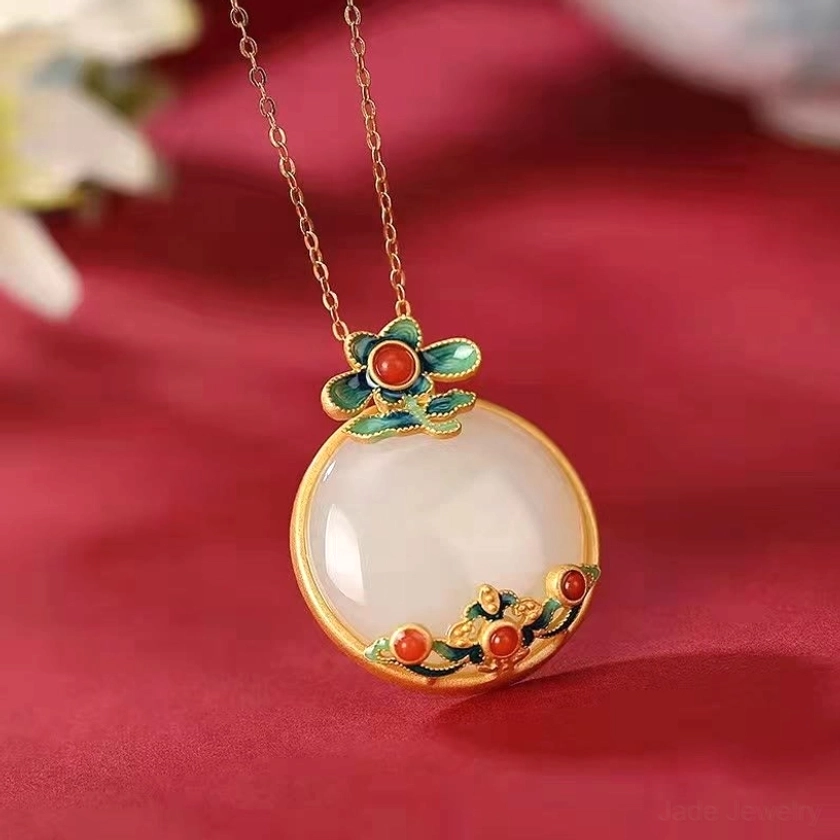 White jade red agate flower pendant necklace side profile showing intricate cloisonné enamel green leaves, red agate beads, hand-polished jade centerpiece, and gold bezel against red silk fabric background