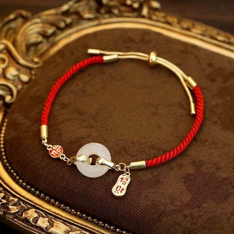 Handcrafted white jade blessing bracelet featuring round jade bead and red cord on ornate gold-trimmed tray