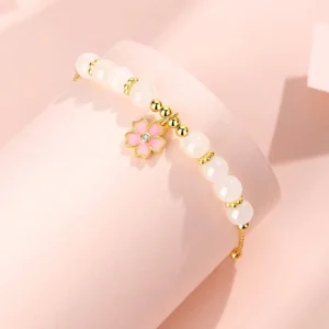 Close-up side view of cherry blossom jade bracelet showing gold-toned silver spacers, smooth white jade beads, and delicate pink enamel flower charm on display stand