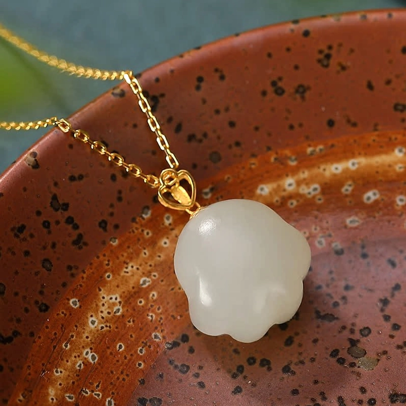 Hetian white jade cat paw pendant necklace side close-up on dark red ceramic bowl showing nephrite texture and gold-plated chain