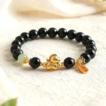 Year of the Horse jade bracelet with black obsidian and red agate beads, gold horse charm, and peace blessing tag on linen
