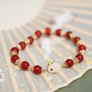 Year of the Rabbit red agate white jade bracelet with gold spacers and rabbit charm, displayed flat on traditional Chinese fabric