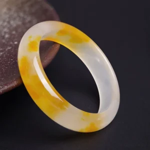 Yellow chalcedony bangle bracelet with golden speckles, oblique top view showcasing semi-translucent stone texture on dark minimalist background