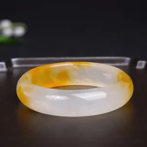 Yellow chalcedony jade bangle side angle with white flowers, displaying smooth rounded edges and natural two-tone coloring
