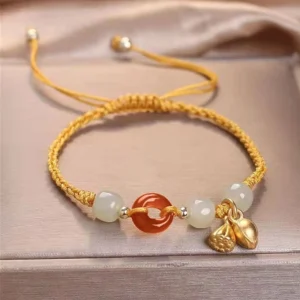Yellow braided cord peace buckle jade bracelet with gold lotus pendant and red agate beads flat lay