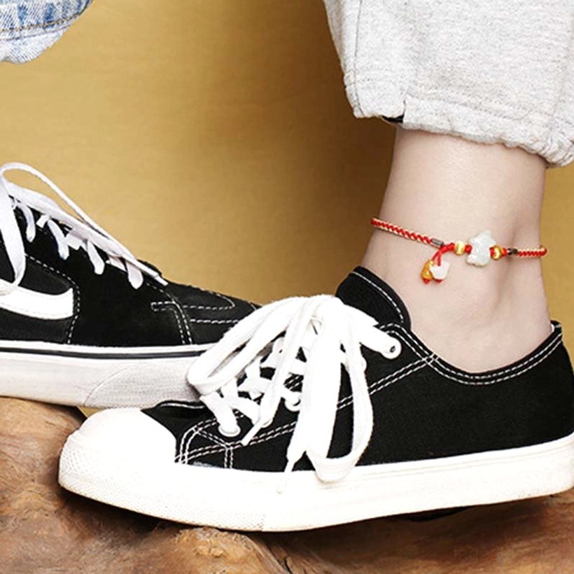 Red string jade anklet worn on ankle with casual black sneakers, showing comfortable everyday wear styling