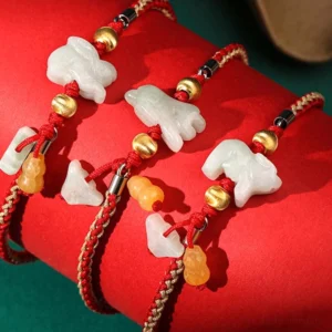 Multiple zodiac jade bracelets with red cord and mixed jade charms displayed on bright red fabric, showing different zodiac animal designs
