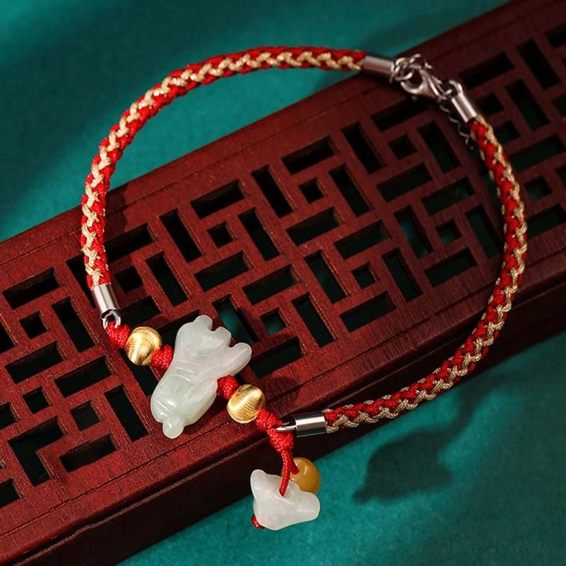 White jade zodiac animal charm bracelet with dual colored jade pendants and braided red rope on traditional wooden lattice display